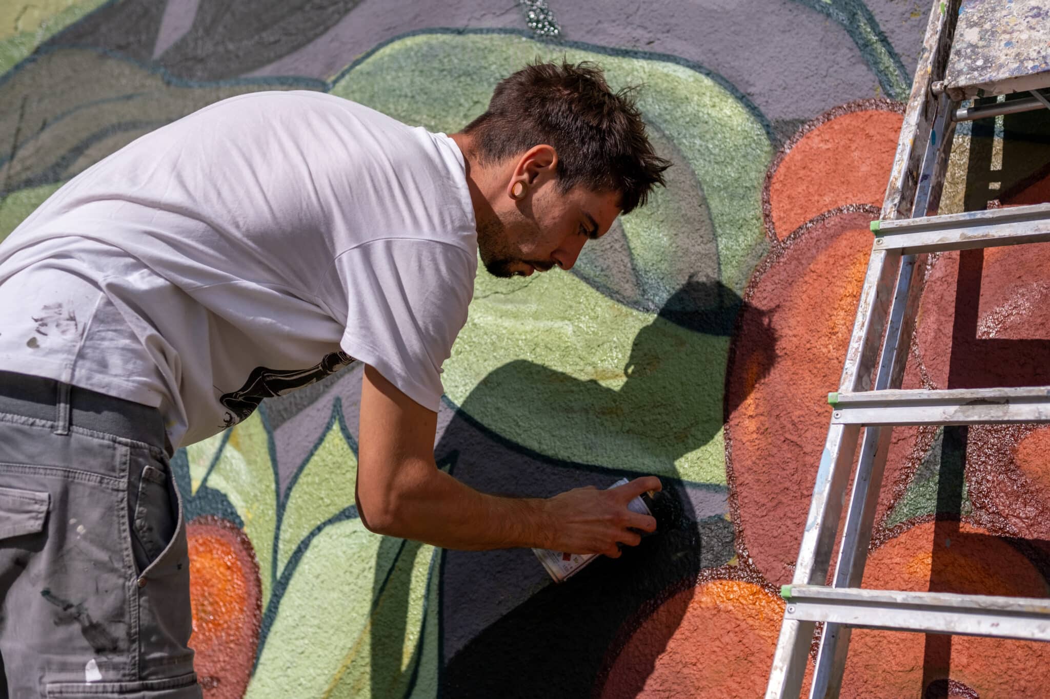 A graffiti artist paints graffiti on a large retaining wall.