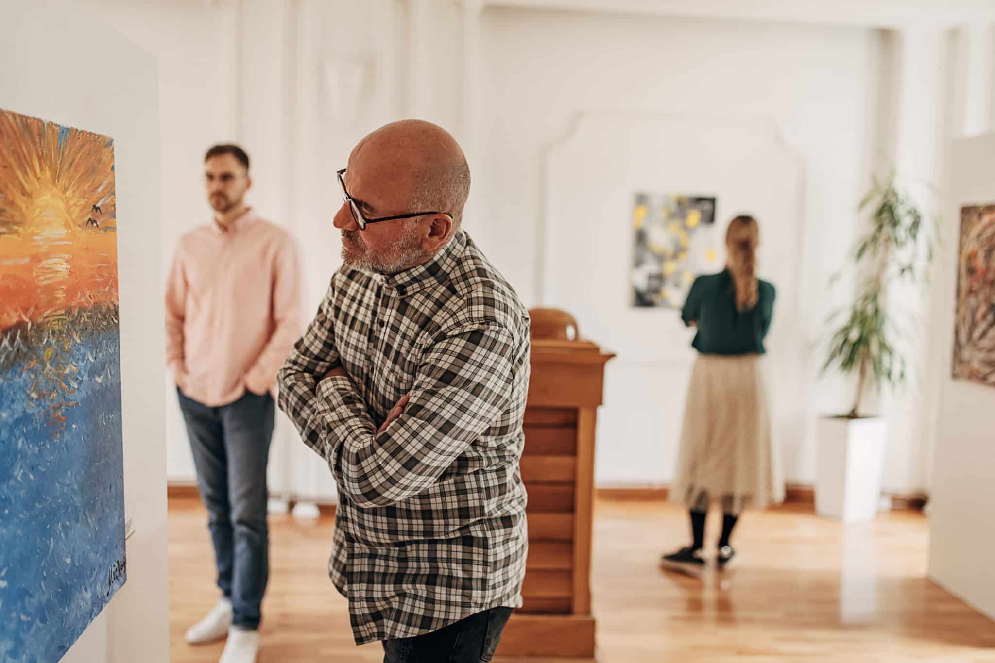 Diverse group of visitors in modern art gallery looking at paintings.